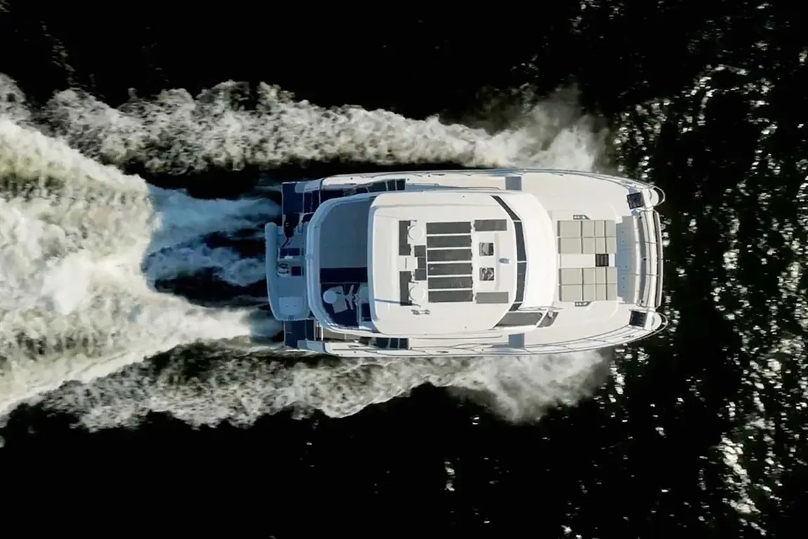 Aerial view of a motorboat cruising on water, leaving a wake; features solar panels and spacious deck seating.